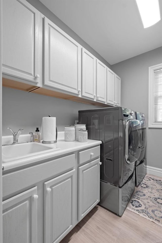 laundry room featuring light wood-type flooring, cabinets, washer and clothes dryer, and sink