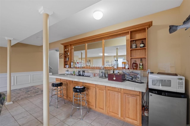 bar with light tile patterned floors, sink, stainless steel refrigerator, and tile countertops