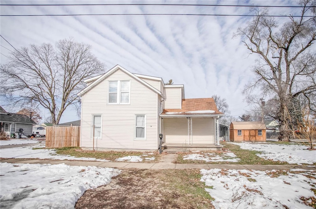 snow covered rear of property with covered porch and a shed