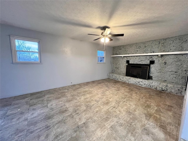 unfurnished living room with a textured ceiling, a fireplace, ceiling fan, and plenty of natural light