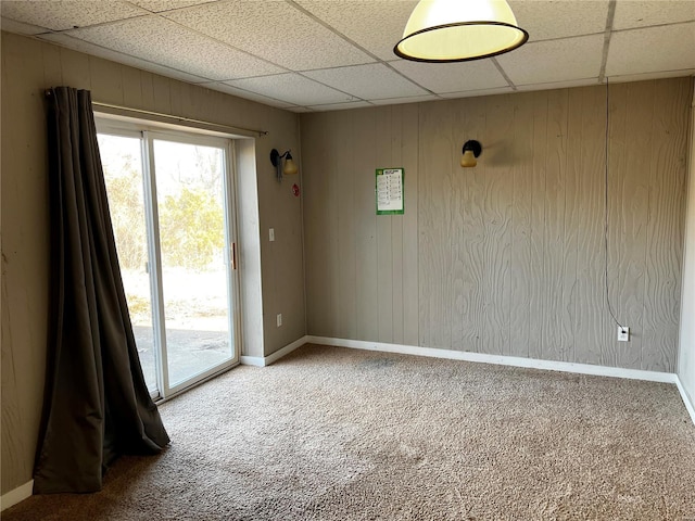 spare room with carpet floors, a drop ceiling, and wooden walls