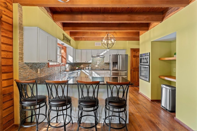 kitchen with white cabinetry, kitchen peninsula, appliances with stainless steel finishes, a breakfast bar, and beamed ceiling