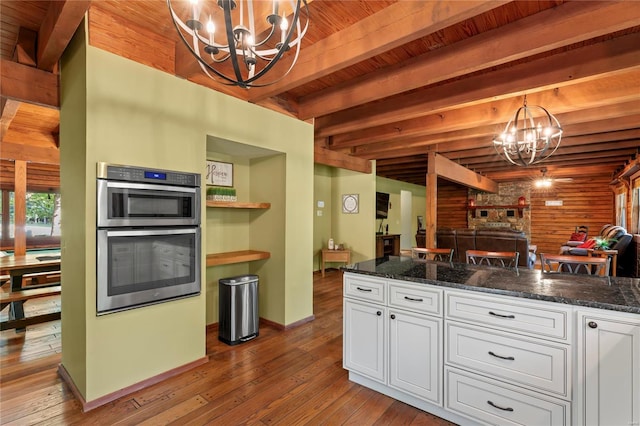 kitchen with a notable chandelier, wood walls, beamed ceiling, hanging light fixtures, and white cabinets