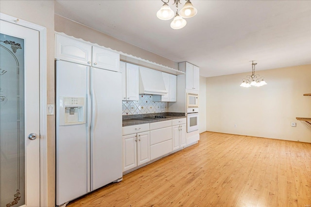 kitchen featuring custom exhaust hood, white cabinetry, an inviting chandelier, decorative light fixtures, and white appliances