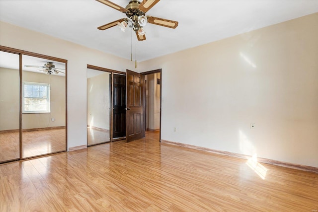 unfurnished bedroom featuring ceiling fan, light hardwood / wood-style floors, and multiple closets