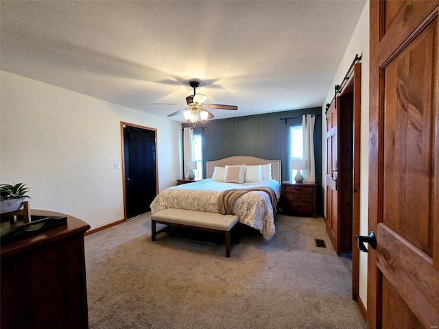 bedroom featuring ceiling fan, a barn door, and light carpet