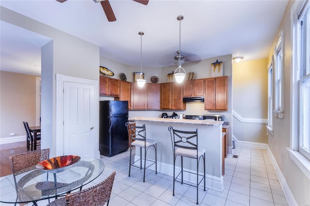 kitchen featuring pendant lighting, a center island, black refrigerator, a breakfast bar, and light tile patterned floors