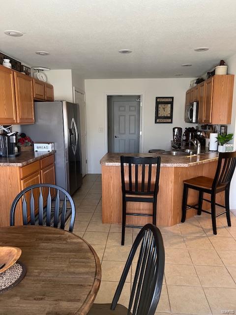 kitchen with stainless steel appliances, a breakfast bar, light tile patterned floors, and kitchen peninsula