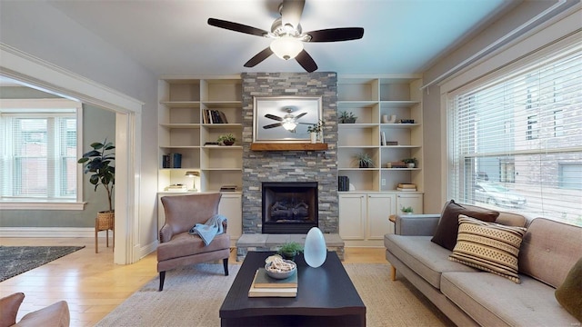 living room with ceiling fan, built in features, a fireplace, and light hardwood / wood-style floors