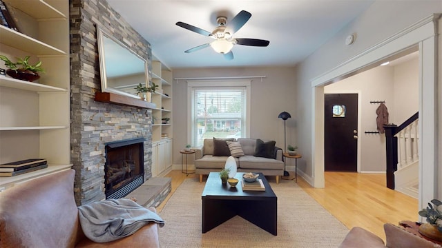 living room featuring ceiling fan, built in features, a stone fireplace, and light hardwood / wood-style floors