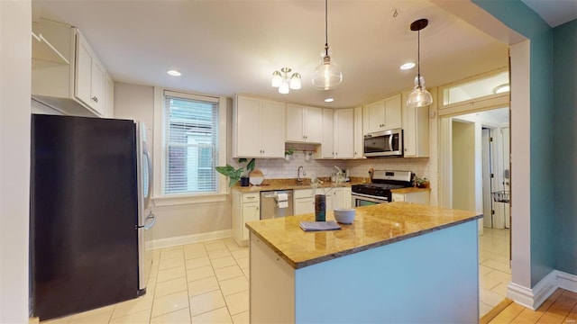 kitchen featuring backsplash, decorative light fixtures, stainless steel appliances, white cabinets, and light stone countertops