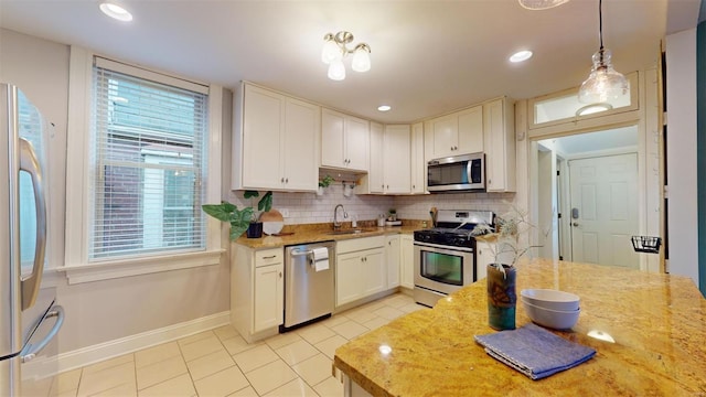 kitchen with appliances with stainless steel finishes, decorative light fixtures, white cabinetry, backsplash, and light stone counters