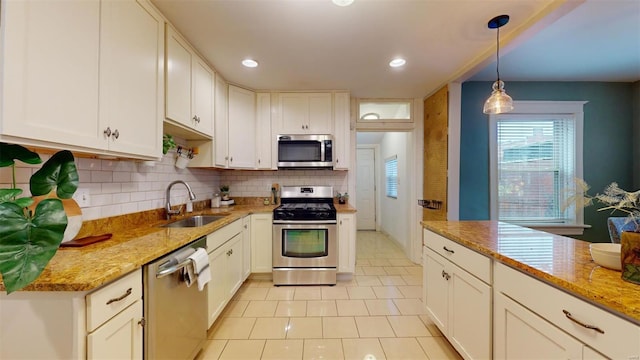 kitchen with pendant lighting, white cabinetry, stainless steel appliances, sink, and light stone counters