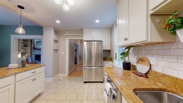 kitchen with hanging light fixtures, light stone countertops, white cabinets, stainless steel fridge, and backsplash