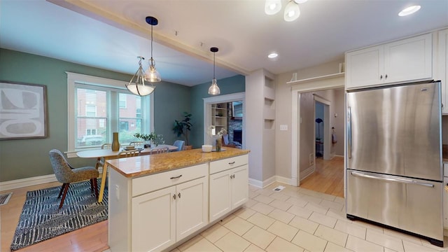 kitchen with decorative light fixtures, light stone countertops, white cabinetry, and stainless steel refrigerator