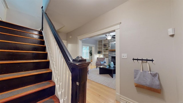 staircase featuring hardwood / wood-style flooring, ceiling fan, and a stone fireplace