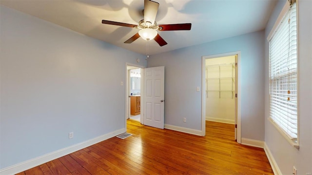 unfurnished bedroom featuring a spacious closet, a closet, ceiling fan, and light wood-type flooring