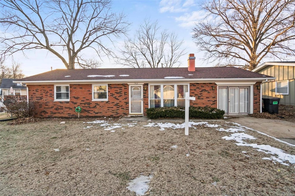 ranch-style home with brick siding, a chimney, and a shingled roof