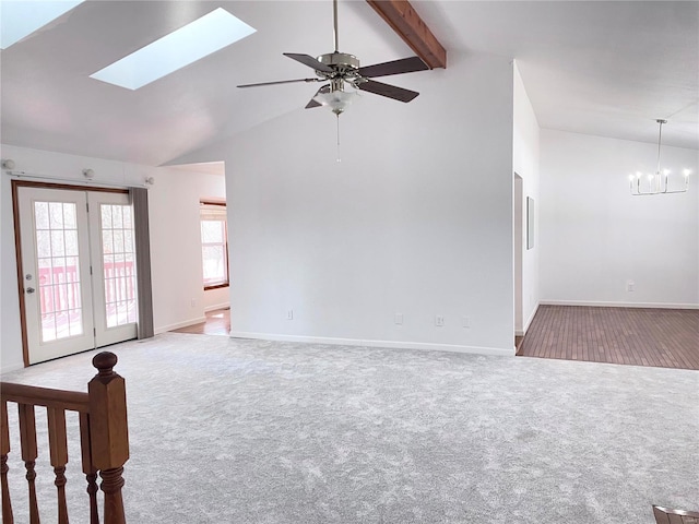 unfurnished living room with ceiling fan with notable chandelier, vaulted ceiling with skylight, and carpet flooring