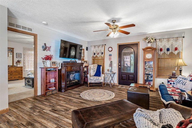 living room featuring ceiling fan, a fireplace, a textured ceiling, and hardwood / wood-style flooring