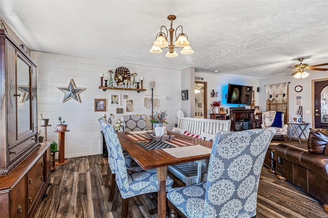 dining space with ceiling fan with notable chandelier, a textured ceiling, dark hardwood / wood-style floors, and wooden walls