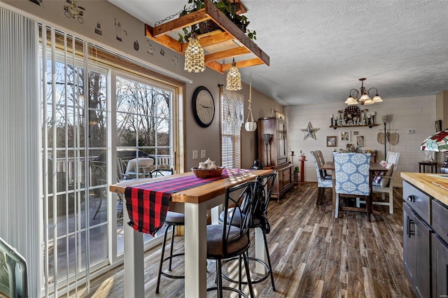 dining area with a textured ceiling, dark wood-type flooring, a chandelier, and beamed ceiling