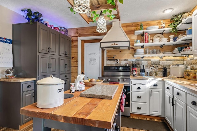 kitchen featuring stainless steel range with electric cooktop, white cabinetry, butcher block countertops, and custom range hood