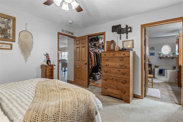 carpeted bedroom with ceiling fan, connected bathroom, a closet, a textured ceiling, and a walk in closet