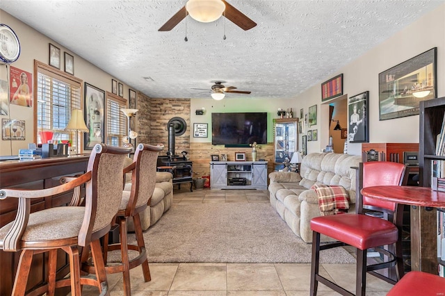 tiled living room featuring ceiling fan, a wood stove, a textured ceiling, and wood walls