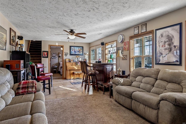 living room with ceiling fan, light tile patterned flooring, bar, and a textured ceiling