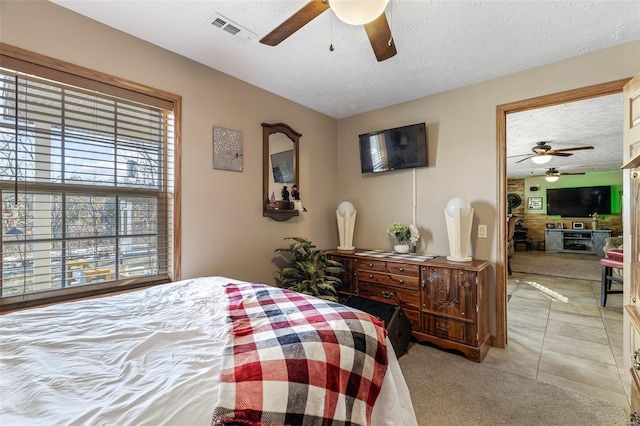 bedroom featuring ceiling fan, multiple windows, light tile patterned floors, and a textured ceiling