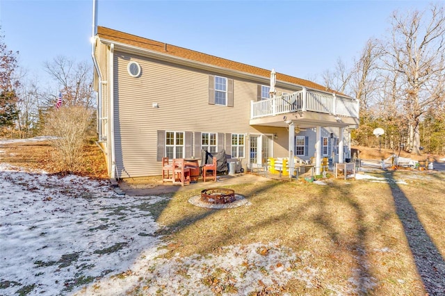 snow covered house with a balcony, an outdoor fire pit, and a yard