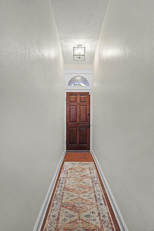 doorway to outside featuring brick floor, baseboards, a textured ceiling, and an inviting chandelier