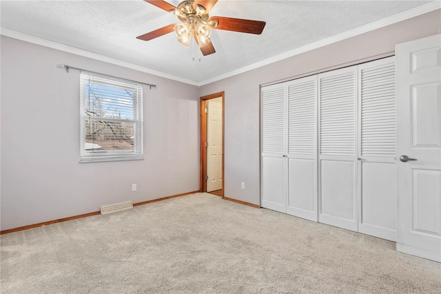 unfurnished bedroom with light colored carpet, ceiling fan, crown molding, a textured ceiling, and a closet