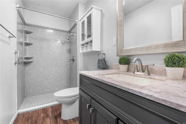 bathroom with hardwood / wood-style flooring, tiled shower, vanity, a textured ceiling, and toilet