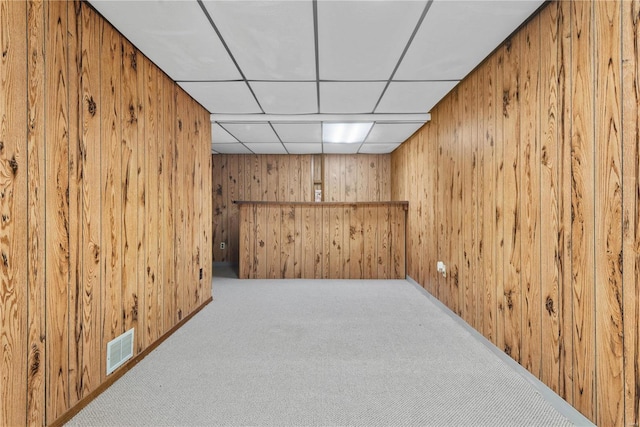 basement featuring carpet flooring, a drop ceiling, and wooden walls