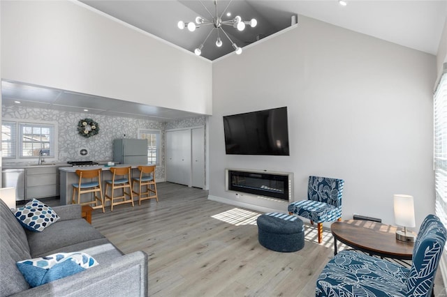 living room featuring sink, a chandelier, light hardwood / wood-style flooring, and high vaulted ceiling