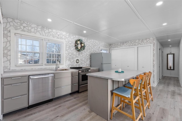 kitchen with appliances with stainless steel finishes, a kitchen island, sink, light wood-type flooring, and a breakfast bar