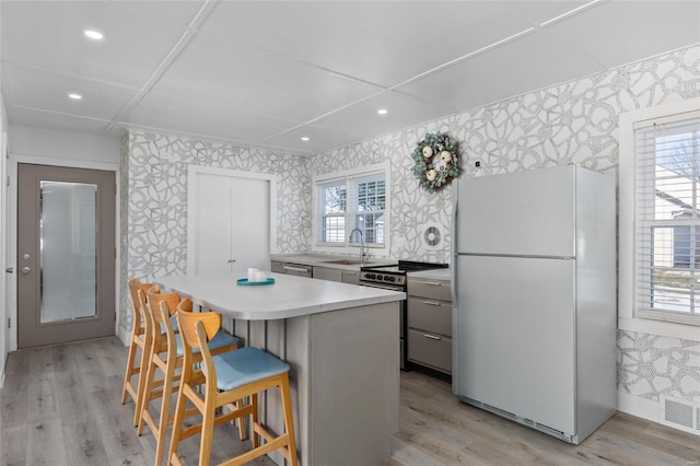 kitchen featuring a center island, a kitchen bar, stainless steel stove, light wood-type flooring, and white refrigerator