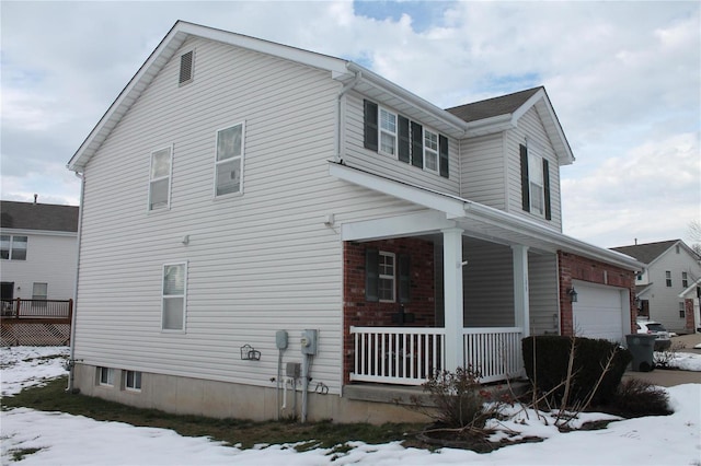 view of snow covered exterior featuring covered porch and a garage