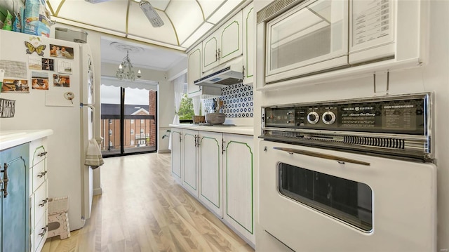 kitchen featuring white appliances, decorative light fixtures, a chandelier, and light wood-type flooring