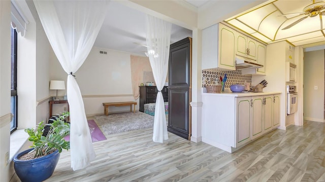 kitchen with wall oven, backsplash, crown molding, and light wood-type flooring