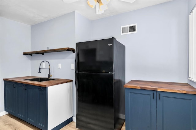 kitchen featuring light hardwood / wood-style floors, blue cabinets, sink, black fridge, and butcher block countertops