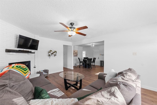 living room featuring ceiling fan, a fireplace, dark hardwood / wood-style floors, and a textured ceiling