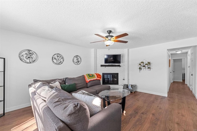 living room with a brick fireplace, hardwood / wood-style floors, a textured ceiling, and ceiling fan