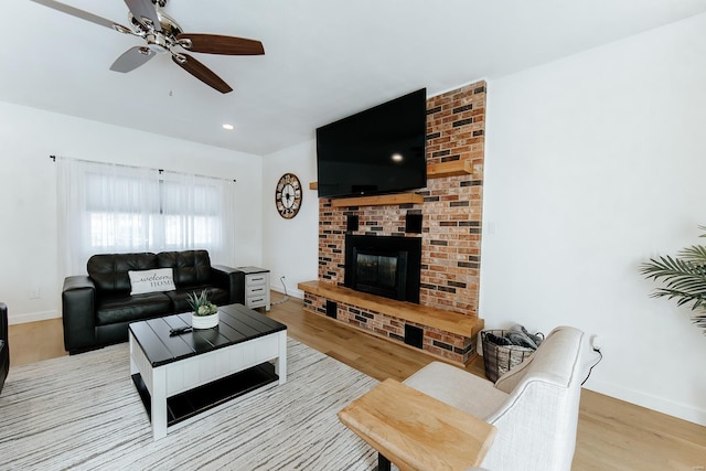 living room featuring light wood-type flooring, a fireplace, baseboards, and ceiling fan