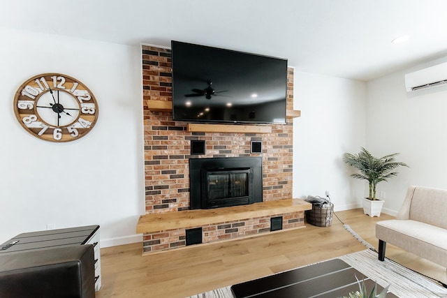 living area with baseboards, a ceiling fan, wood finished floors, a wall mounted air conditioner, and a brick fireplace