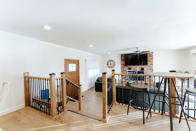 interior space with recessed lighting, a fireplace, wood finished floors, a ceiling fan, and a wall mounted air conditioner