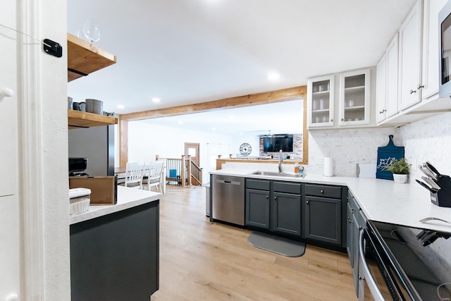 kitchen featuring a sink, light wood-style floors, light countertops, appliances with stainless steel finishes, and glass insert cabinets