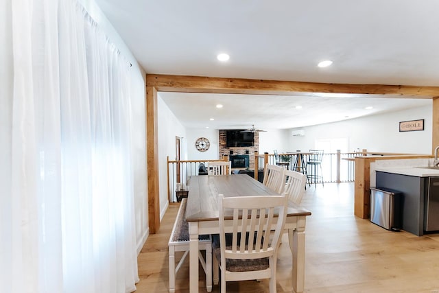 dining room with recessed lighting, a fireplace, beam ceiling, and light wood-style floors